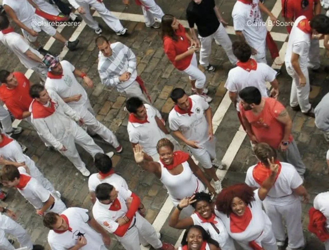 An aerial view of the crowd in white and red at the Running of the Bulls festival in Pamplona, Spain, with Claire B. Soares waving up at the camera.